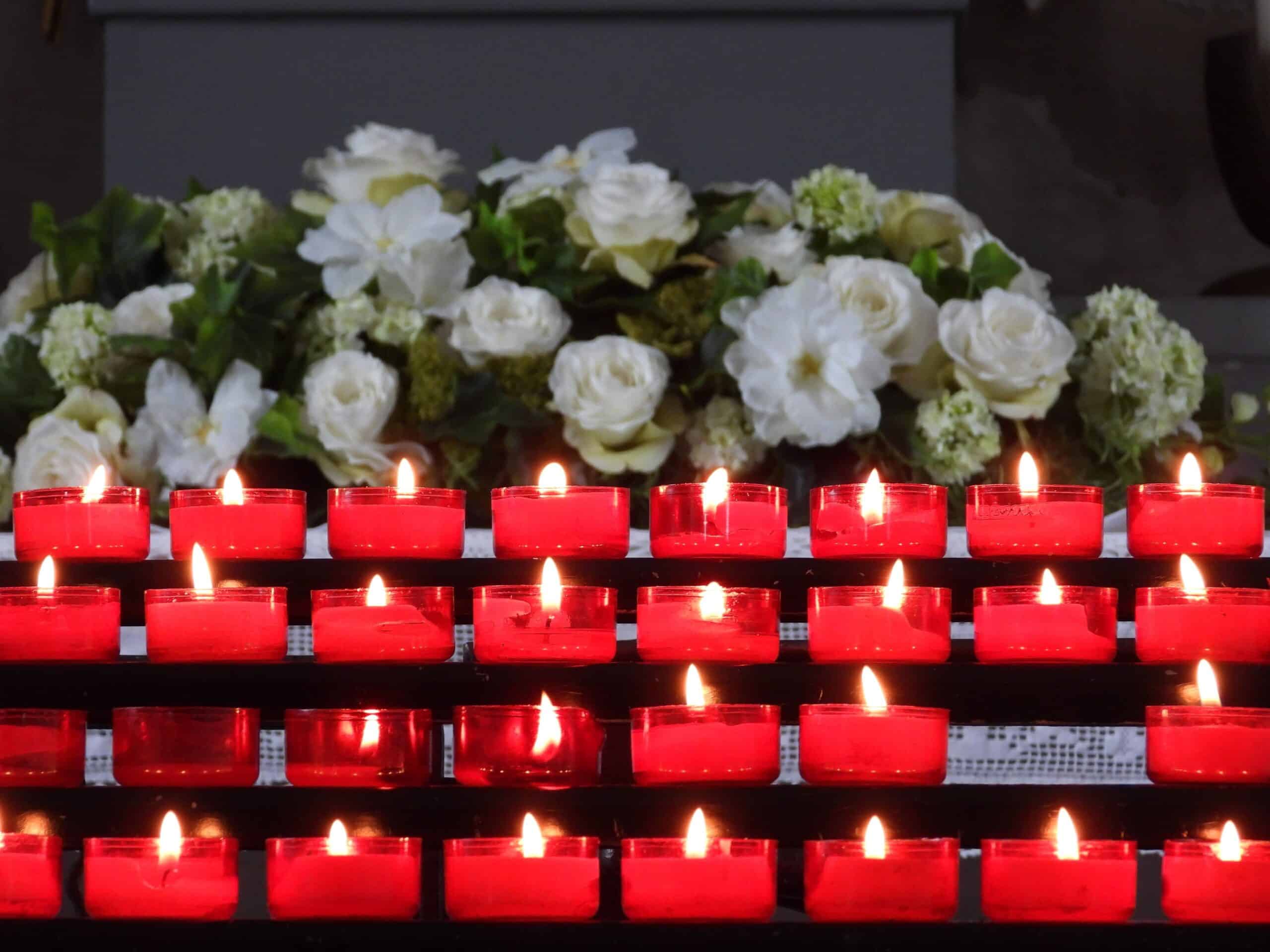 A serene arrangement of lit red candles with white flowers in the background, creating a peaceful ambiance.